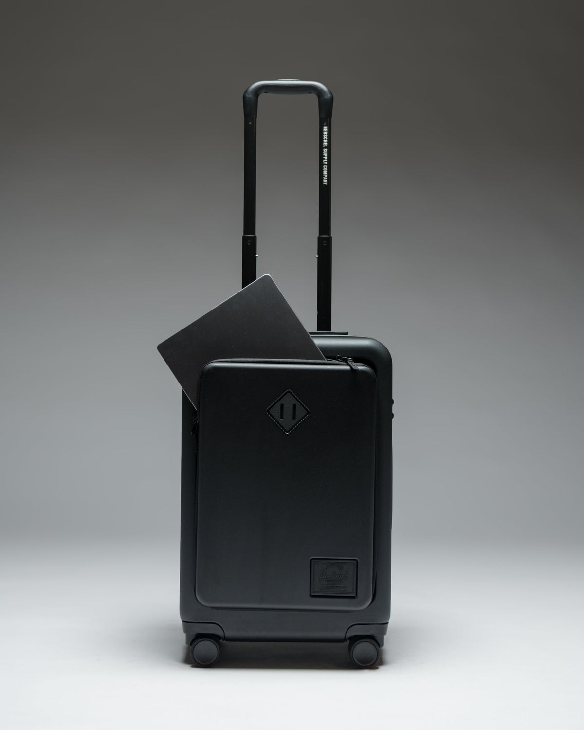 Herschel Heritage Hardshell Pro Large Carry On luggage in Black, shown from the front with a textured hard shell and retractable handle.