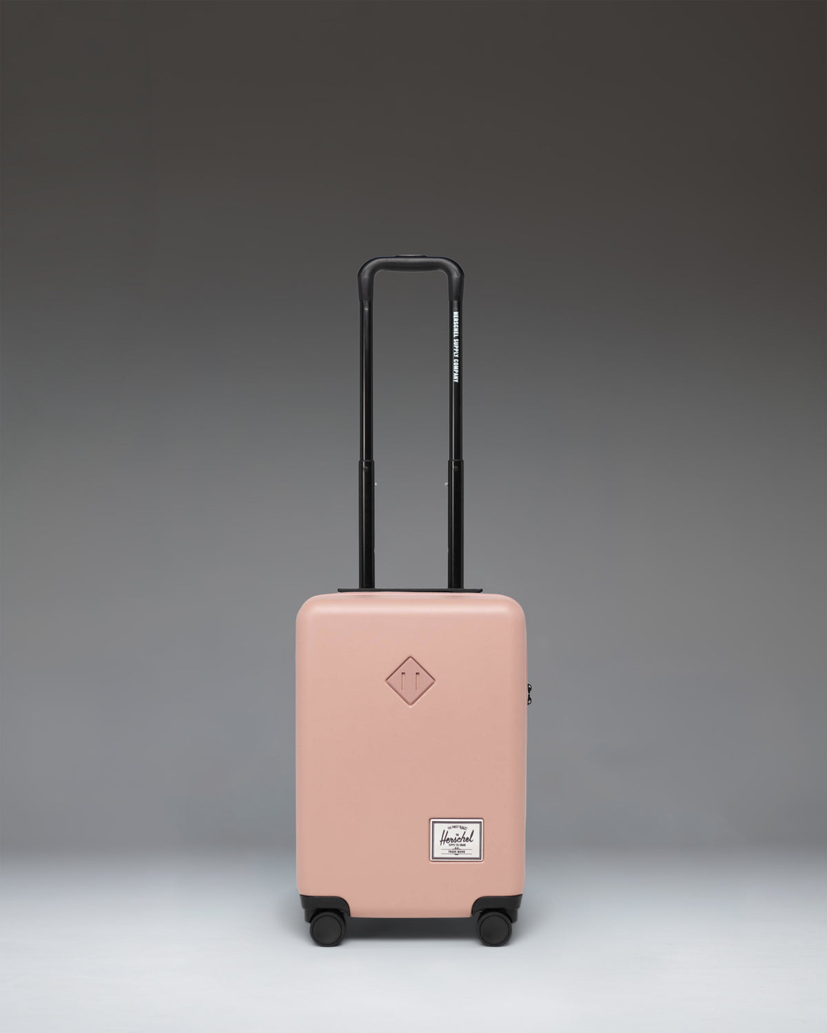 Herschel Heritage Hardshell Carry On Luggage in Ash Rose. Front view of the durable hard shell suitcase with wheels and a retractable handle.