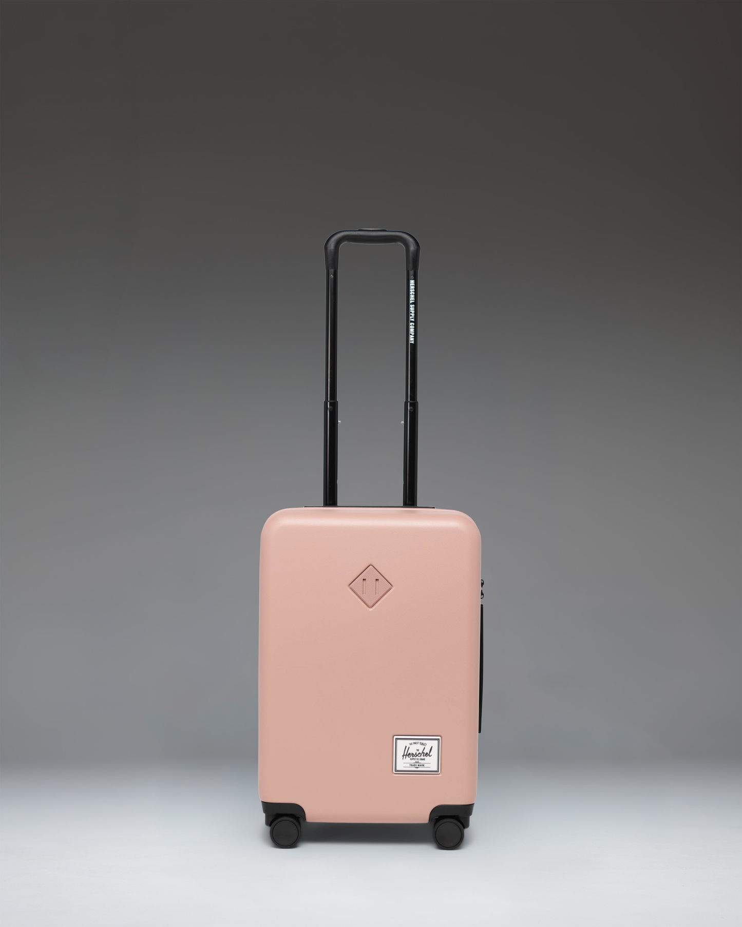 Herschel Heritage Hardshell Large Carry-On Luggage in Ash Rose pink, featuring a durable textured exterior, telescopic handle, and multi-directional wheels.