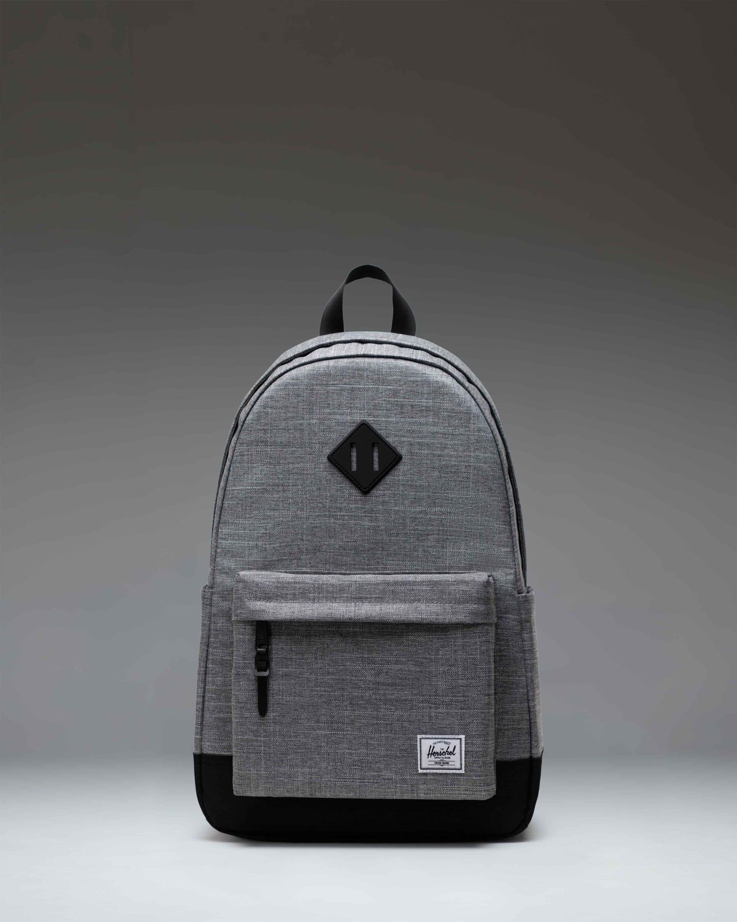 Herschel Heritage Backpack in Raven Crosshatch, showing a front view with a gray fabric, a brown diamond accent, and a black front pocket.