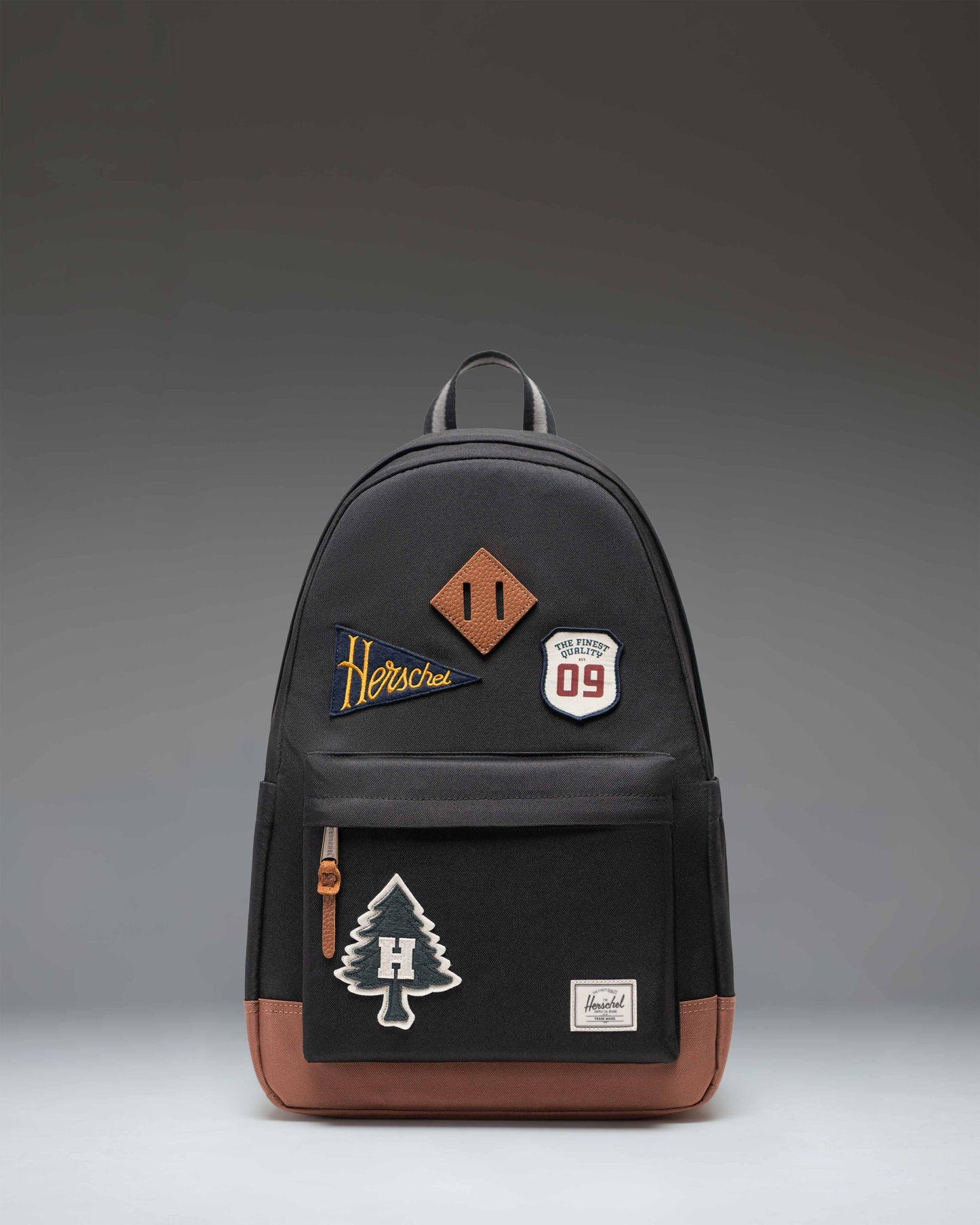 Herschel Heritage backpack in black, featuring distinct patches including a floral pattern and text graphics.