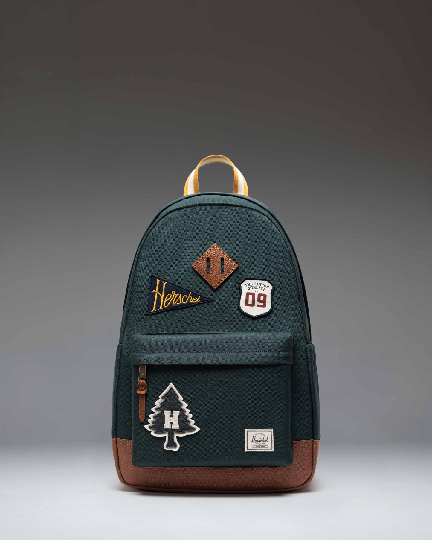 Herschel Heritage Backpack in Patches Green Gables, featuring a green base with various stitched-on patches and a brown diamond accent.