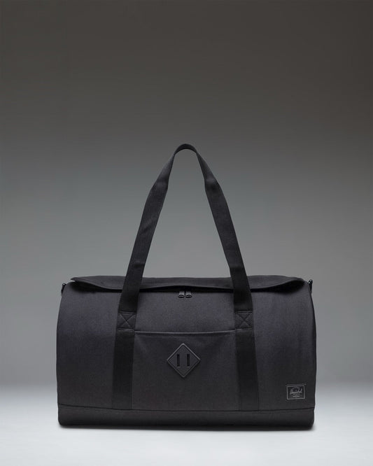 Herschel Heritage Duffle bag in Black Tonal, showing the front profile with a clean design, dual carrying handles, and a signature woven label.
