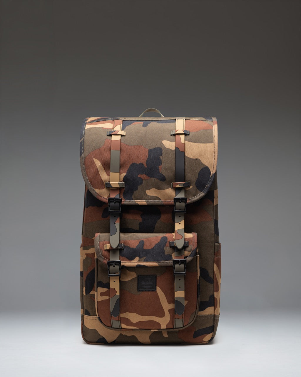 Herschel Little America Backpack in Woodland Camo with black rubber straps and a black classic label on the front pocket.