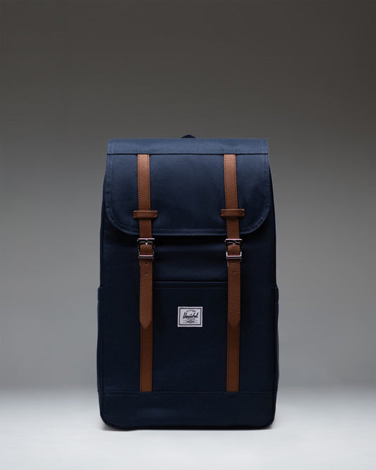 Herschel Retreat Backpack in navy blue, featuring a classic cinch-top design with dual brown strap closures and a front storage sleeve.