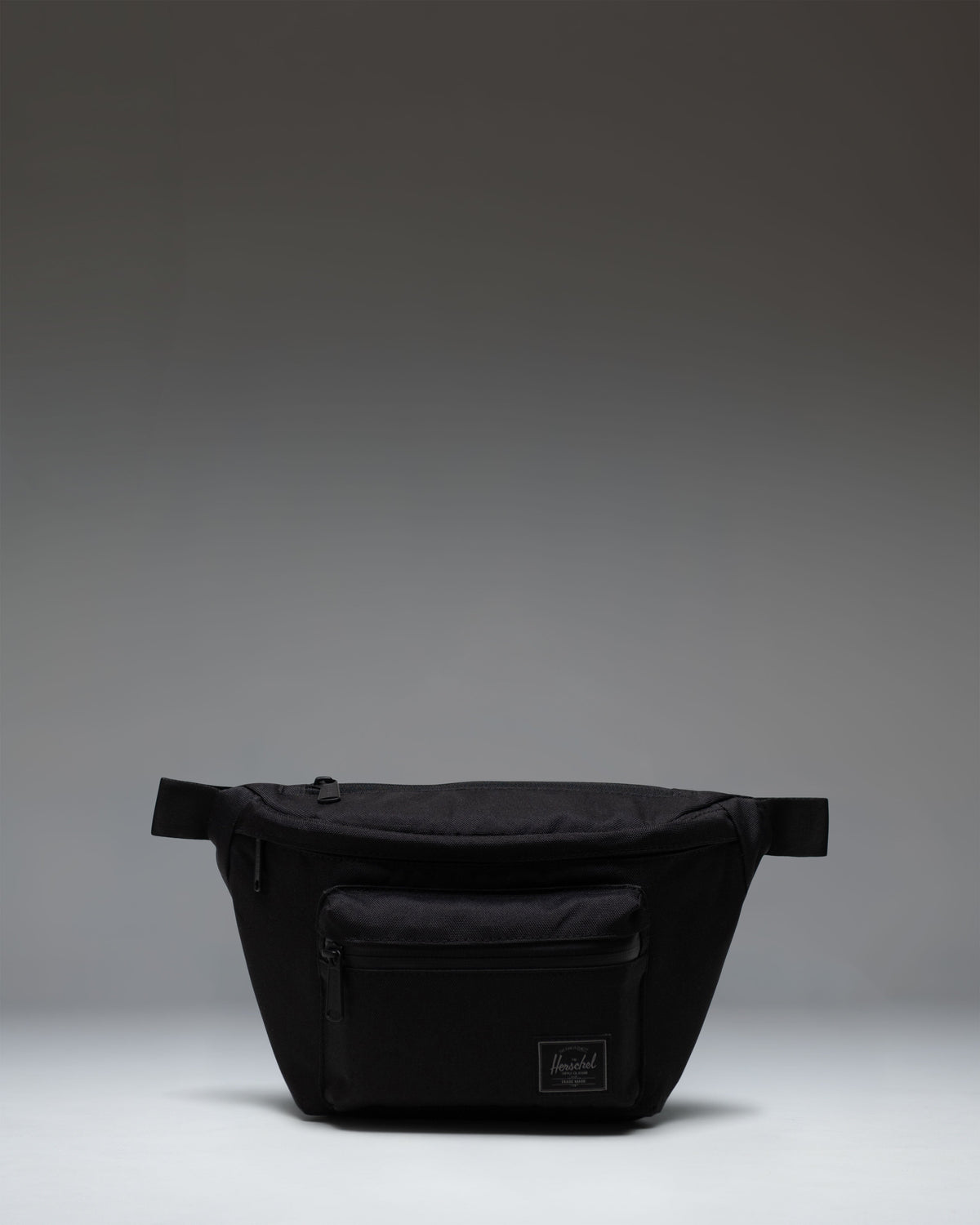 Herschel Supply Co Pop Quiz Hip Pack in Black Tonal, showing the front view of the sleek, compact waist bag with zipper detail.