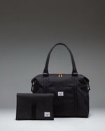Herschel Supply Co. Strand Duffle Diaper Bag in black, featuring top handles, a removable shoulder strap, and front storage sleeves.