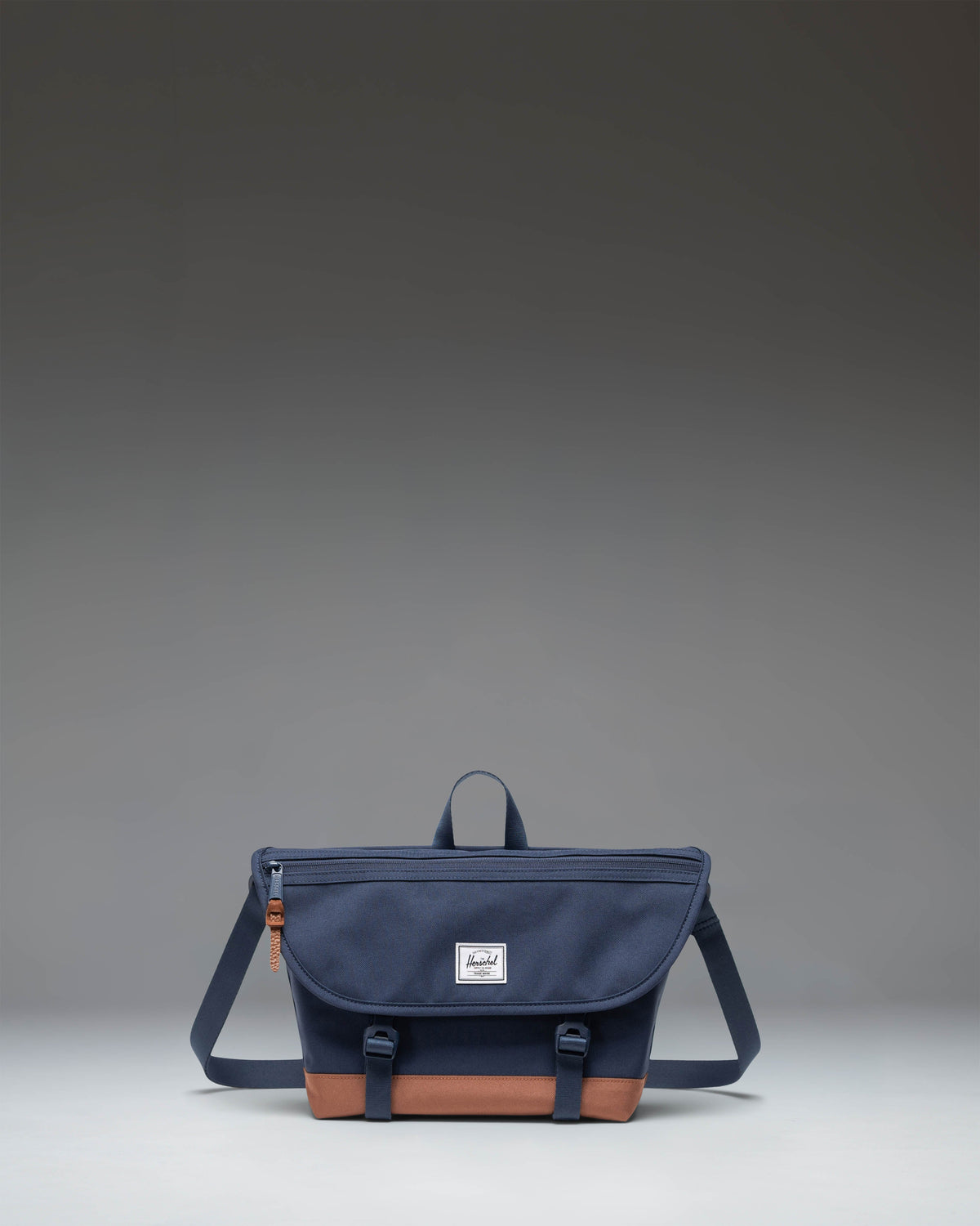Herschel Supply Co Cove Small Messenger bag in Navy and Saddle Brown, showing a front view with the main flap and strap.