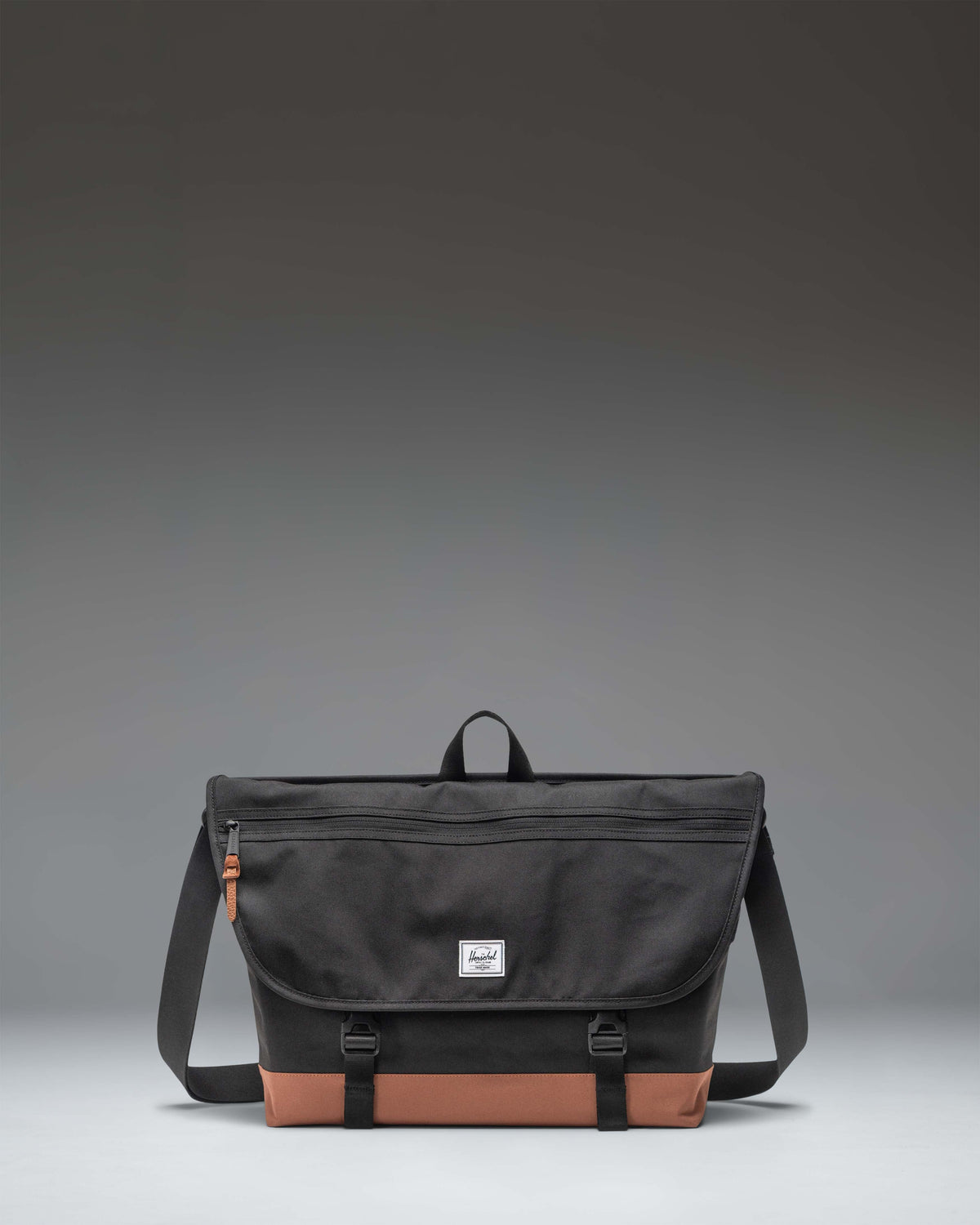 Herschel Supply Co. Cove Messenger bag in Black/Saddle Brown featuring a main compartment, front pockets, and an adjustable shoulder strap.