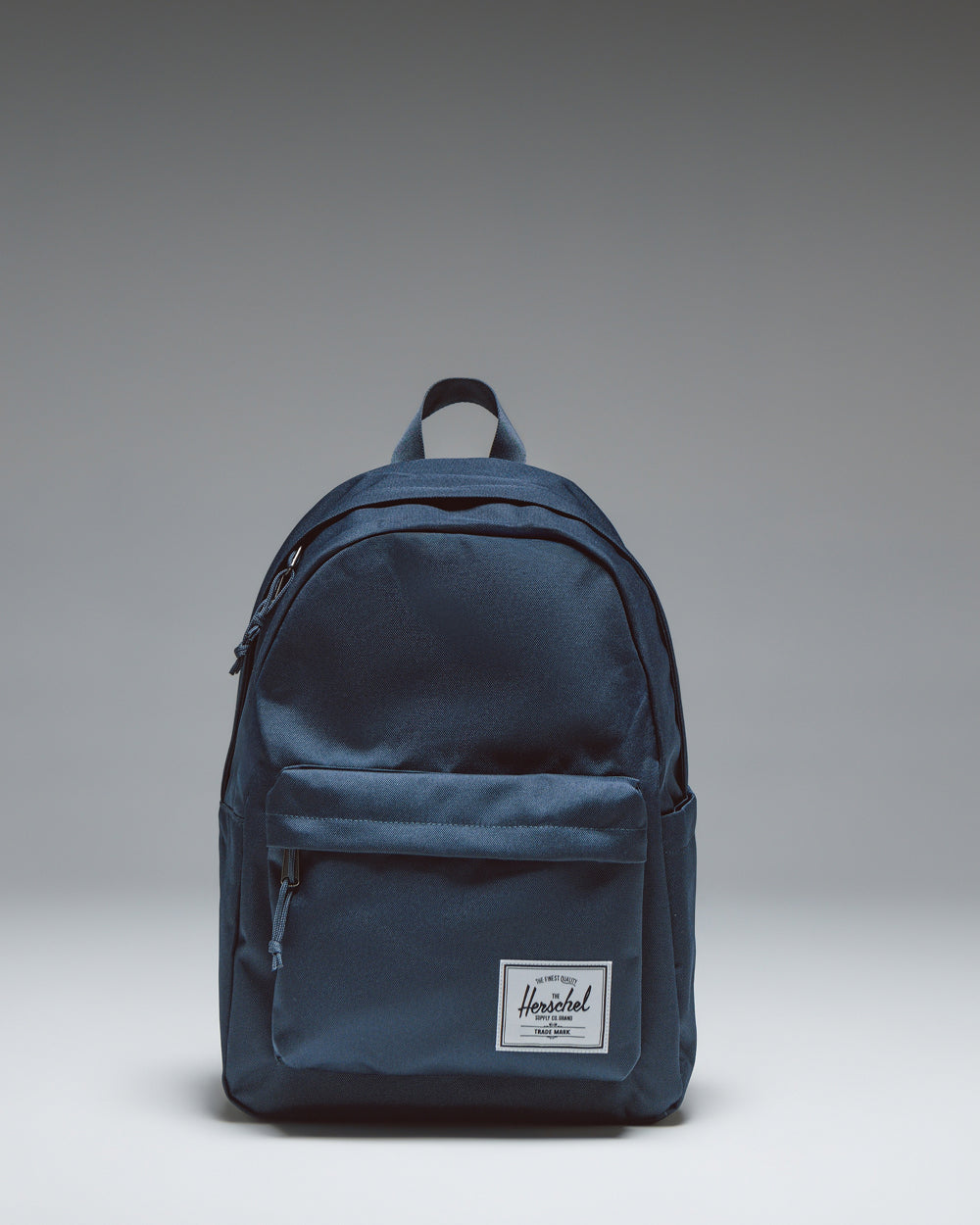 Herschel Classic Backpack in navy blue, featuring a clean, minimalist design with a zippered front pocket and a woven logo label.