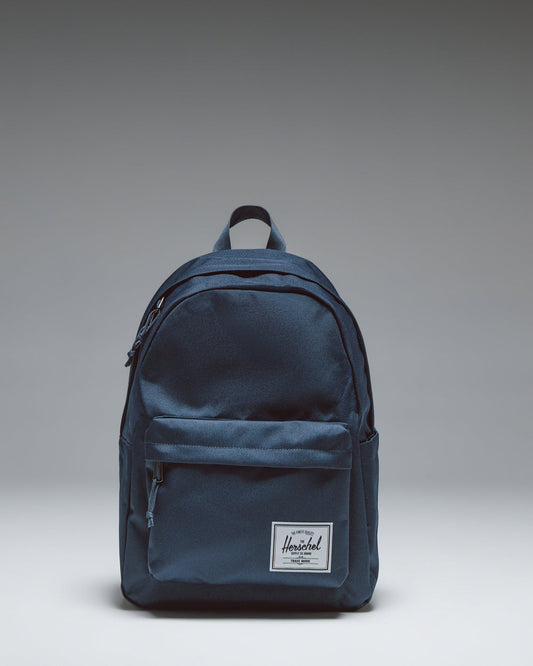 Herschel Classic Backpack in navy blue, featuring a clean, minimalist design with a zippered front pocket and a woven logo label.