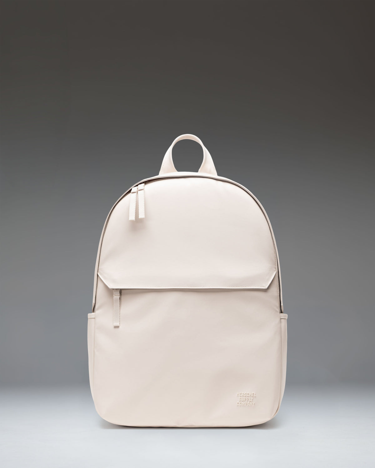 Herschel Supply Co. Alberni Backpack in Moonbeam, showing a front view of the minimalist tan backpack with a top handle and shoulder straps.