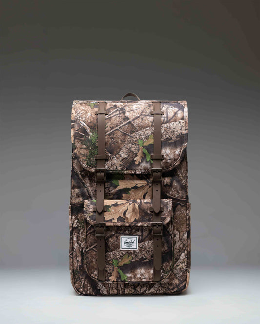 Herschel Little America Backpack in Realtree APX Camo featuring black straps and a front pocket.