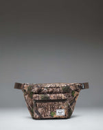 Herschel Supply Co. Pop Quiz Hip Pack in Realtree APX Camo pattern, showing the adjustable strap and front zipper pocket.