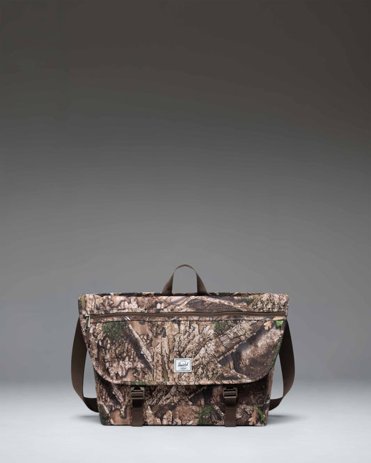Herschel Supply Co. Realtree Cove Messenger bag in Realtree APX Camo pattern, showing the front design with straps and buckles.