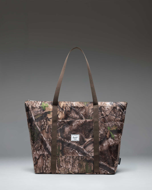 Herschel Supply Co. Portland Packable Tote bag in Realtree APX Camo pattern, showing a woodland camouflage design with leaves and branches.