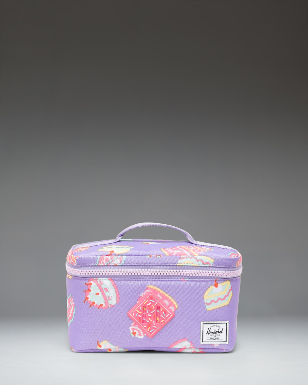 Herschel Supply Co Little Herschel Heritage Lunch Box in Cakes colorway featuring a pattern of colorful cakes and sweet treats.