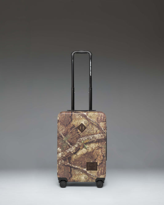 Herschel Heritage Large Carry-On Luggage in Realtree APX Camo pattern, showing the front view of the hard-shell suitcase.