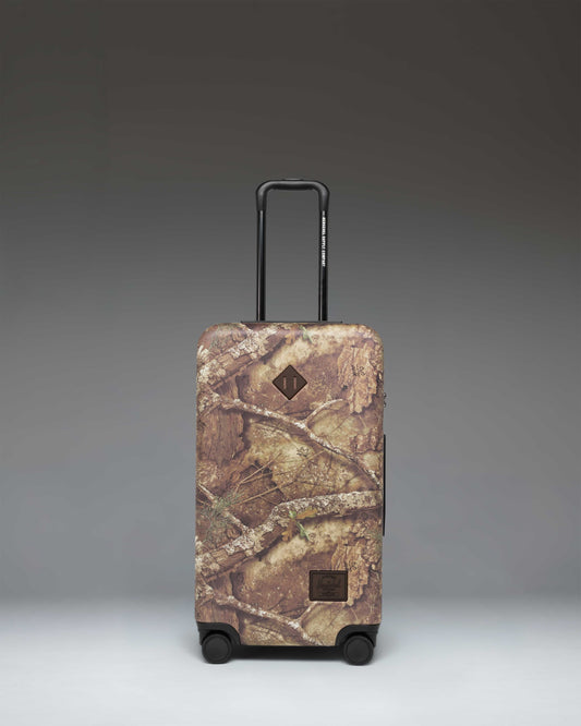 Realtree Herschel Heritage Medium Luggage in Realtree APX Camo pattern, a rolling suitcase featuring a distinct woodland camouflage design.