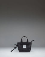 Herschel Supply Co. Heritage Tote Bag Charm in black, featuring a mini zippered tote design with a metal keyring and clip attachment.