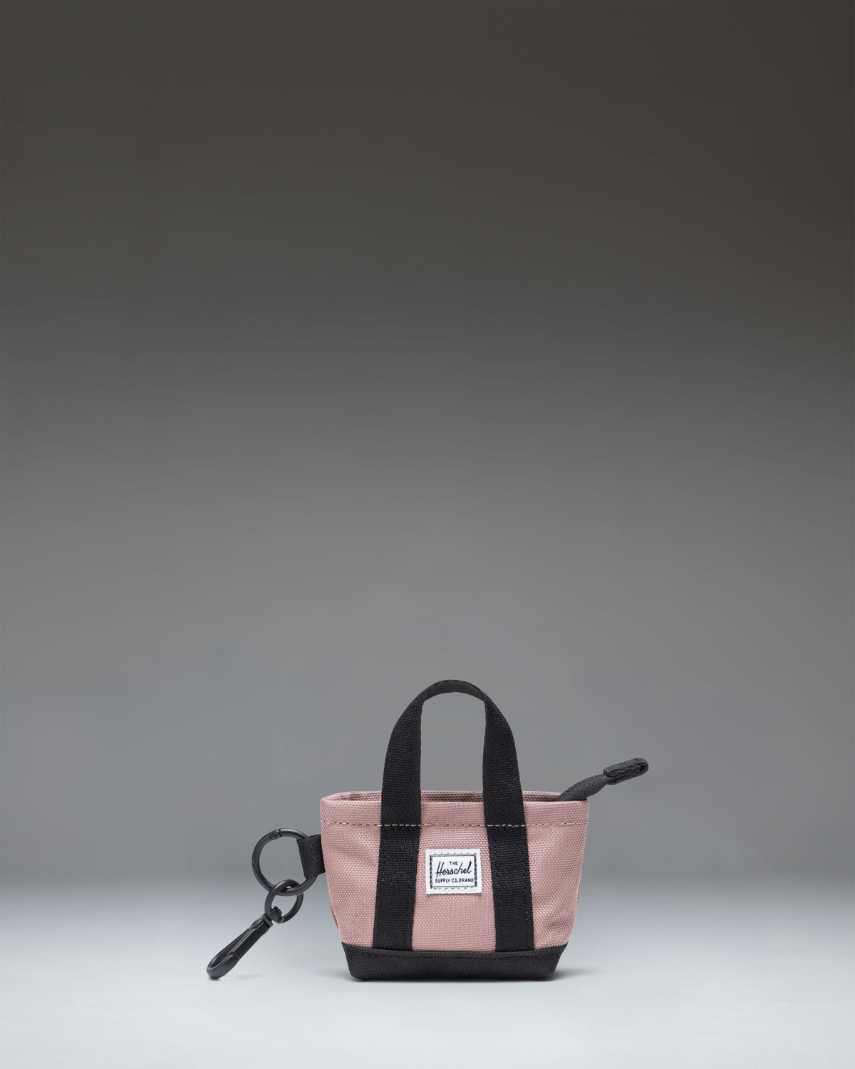 A miniature Herschel Heritage Tote Bag Charm in Ash Rose pink, featuring a classic design with dual top handles and a front storage sleeve.