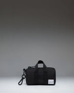 Herschel Novel duffle bag charm in black, showing a miniature version of the classic duffle bag with a zipper closure and top handles.