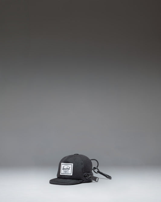 Herschel Supply Co. Sylas Classic Cap Bag Charm in black, showing the front view of a miniature baseball cap keychain accessory.