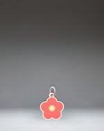 Herschel Daisy Bag Charm in Pink Daisy, featuring a stylized pink daisy flower design with a central yellow disc and attached metal hardware.