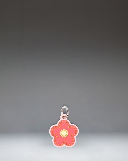 Herschel Daisy Bag Charm in Pink Daisy, featuring a stylized pink daisy flower design with a central yellow disc and attached metal hardware.